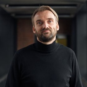 PD Dr Thomas Jacobs: a researcher with short, dark beard, blond longer hair in black clothes against a dark background.