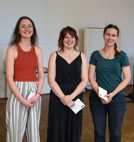 Das Foto zeigt drei Doktorandinnen mit Preisumschlägen in den Händen.