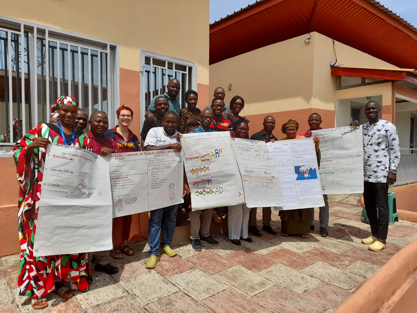 At the end of the 1-week mpox training at CRV-LFVHVG. October 2024, Conakry, Guinea. sixteen laboratory staff with one trainer all standing together with posters after training for a group photo