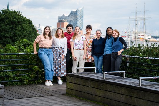 Laborgruppe Fusco: eine Gruppe Forscher und Forscherinnen stehen in einem gläsernen Durchgang und lachen in die Kamera.