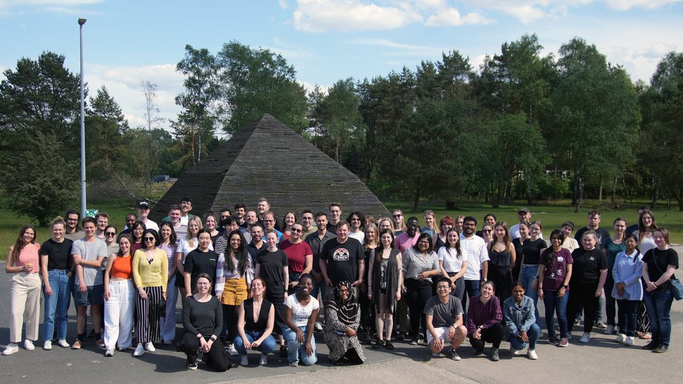 Das Foto zeigt eine Gruppe von circa 80 Nachwuchswissenschaftler:innen auf einem Platz im Freien, Im Hintergrund sind Bäume.