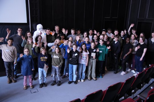 Etwa 30 Jugendliche stehen mit einigen Forscher:innen im Hörsaal vor der Tafel und winken.