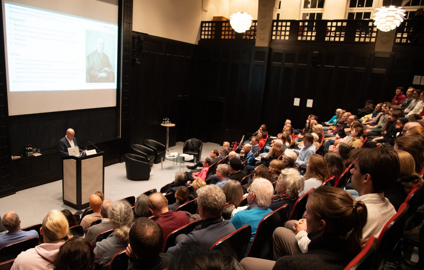 Das Foto zeigt den vollen Hörsaal von schräg links oben. Unten vorn am Pult steht ein Redner.
