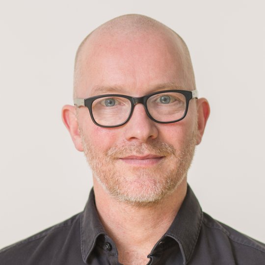 Prof. Dr. Tim Gilberger: der Gruppenleiter trägt eine schwarze Brille, Glatze und ein schwarzes Hemd vor einem weißen Hintergrund.