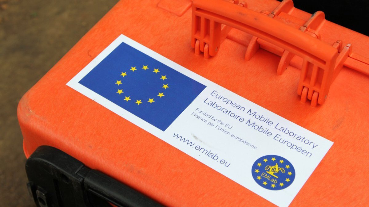 A large orange transporter box with a rectangular EMLab sticker on the front is shown.