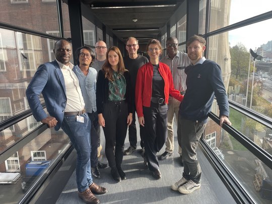 Die Gruppenleitungen der Sektion Implementationsforschung stehen in einem gläsernden Durchgang und lächeln in die Kamera.