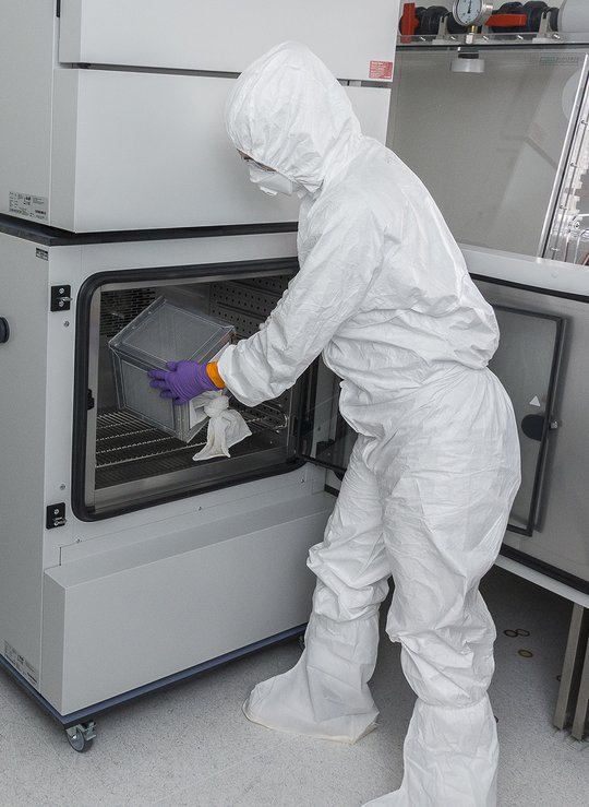A researcher in a full protective suit is seen taking something out of the climate cabinet in a laboratory