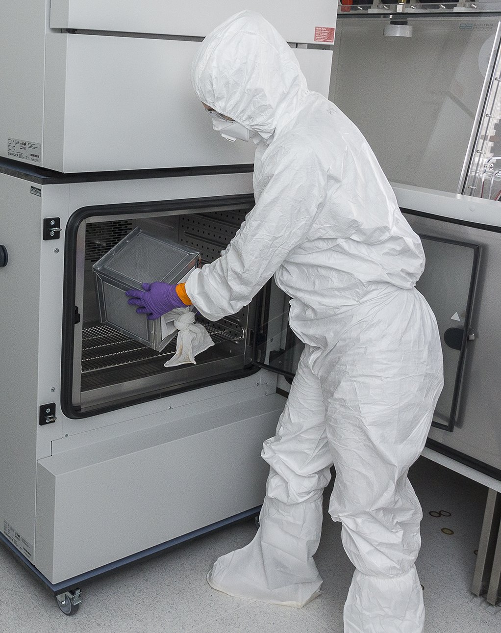 A researcher in a full protective suit is seen taking something out of the climate cabinet in a laboratory
