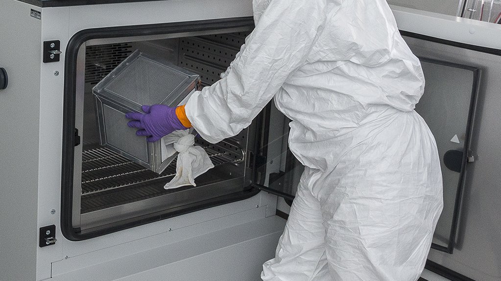 A researcher in a full protective suit is seen taking something out of the climate cabinet in a laboratory