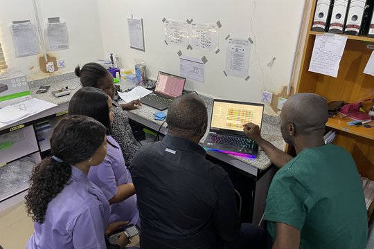 Sequencing lab staff performing bioinformatics analysis of sequencing results to obtain sequences alignments for phylogeny. February 2024, Irrua, Nigeria. Five laboratory staff performing bioinformatic analysis in front of two computers in the lab.