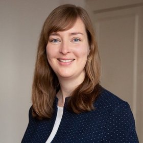 [Translate to English:] Junge lächelnde Frau mit einer Tür im Hintergrund