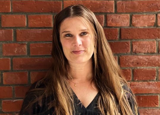 Anna Bachmann: eine Forscherin steht draußen vor einer Backsteinwand und lacht in die Kamera.