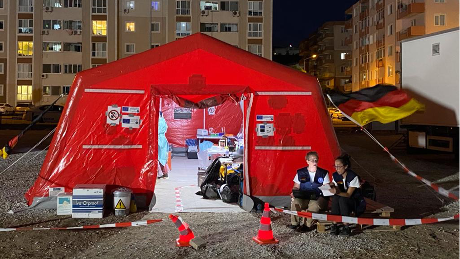 The EMLab has been set up in a large tent. The image is shot in the dark. In the foregound is a large red tent with a brightly lit lab inside. Behind the tent blocks of flats are visible.