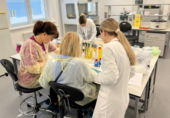 Laborarbeit in Zusammenarbeit mit Wissenschaftlerinnen aus der Ukraine und Moldau Foto mehrerer Wissenschaftlerinnen in Laborkitteln im Labor. Sie sitzen konzentriert um einen Tisch herum.