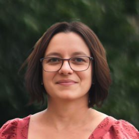 Ph.D. Yaiza Fernández García: Zu sehen ist eine Forscherin die eine dünnrandige Brille, kinnlanges, braunes Haar und eine rosa Bluse trägt.