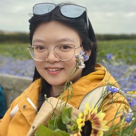 A smiling woman with glasses, a road and some grass in the background
