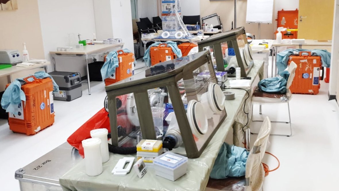 EMLab setup at a regional hospital within the EU during the COVID19 pandemic in 2020. Laboratory setup in a large hospital room with many tables where the mobile laboratory equipment such as glovebox, centrifuges and other workspaces are placed.