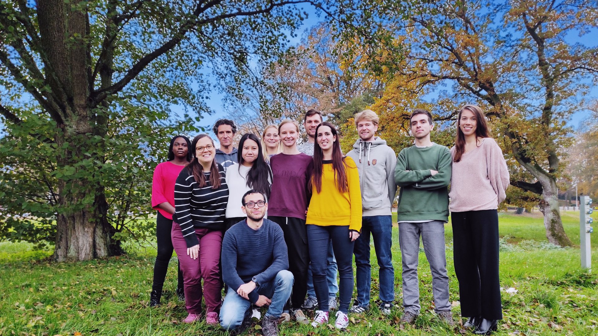 Eine freundliche Gruppe Forscher:innen mit ihrem Forschungsgruppnleiter draußen in einem Park