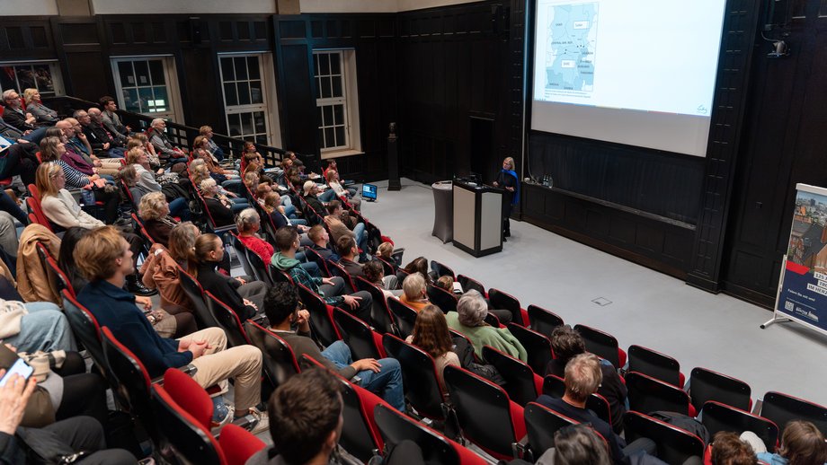 Publikum bei Infoveranstaltung Das Foto zeigt den fast voll besetzten Hörsaal des BNITM. Vorne steht eine Rednerin am Pult, im Hintergrund sieht man eine Folie der Präsentation.