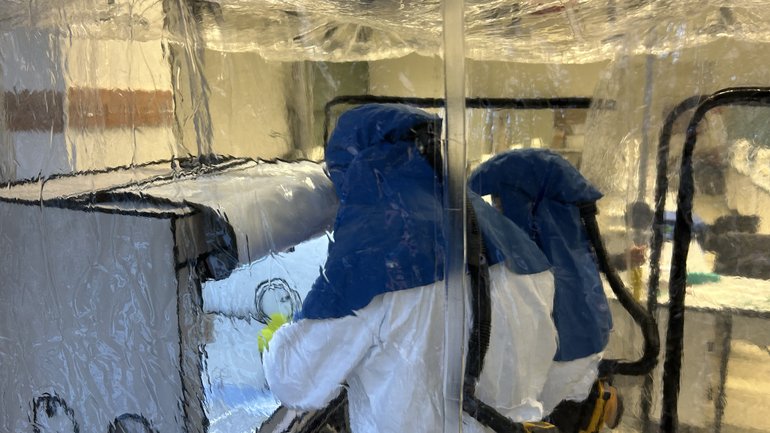 Zwei Personen arbeiten im Schutzanzug in einer abgeschirmten Arbeitsbox