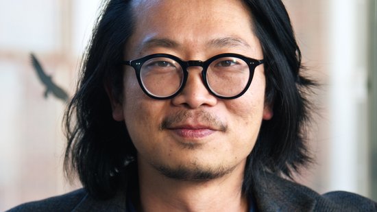 Dr. Sung-Joon Park: ein Forscher der schulterlanges Haar, eine runde schwarze Brille, ein dunkles Sakko über einem dunkelblauen Oberteil trägt.
