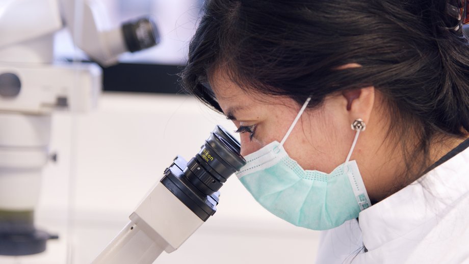 A scientist wearing a face mask at a microscope