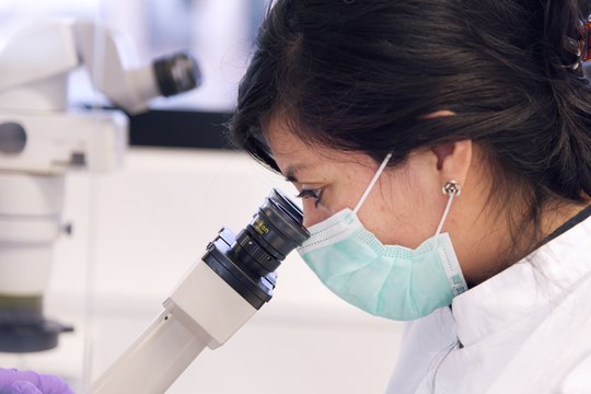 A scientist wearing a face mask at a microscope