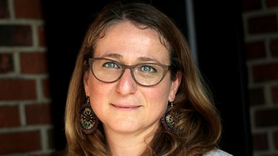 Daniela Fusco, Ph.D. Daniela Fusco, Ph.D.: a researcher in front of a dark red brick background, wearing her blonde shoulder-length hair loose.