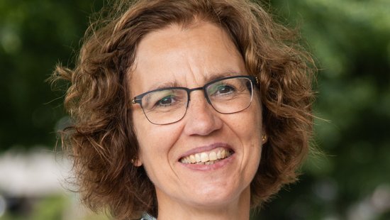 Prof. Dr. Iris Bruchhaus Prof. Iris Bruchhaus, a researcher with a white and blue blouse, curly medium-length hair, glasses and an open smile