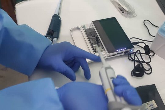 Sequencing lab staff loads a sequencing device for the first run in the newly opened laboratory. Guéckédou, Guinea, December 2025. A sequencing device is being loaded with a pipette from a laboratory staff that is wearing gloves. On the table are also pipette tips and another pipette.