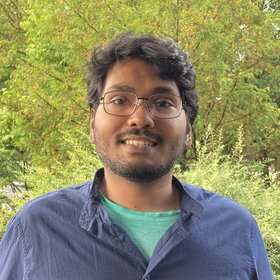 Saleh Yunus Saleh Yunus: A PhD student smiles at the camera. He wears medium length black hair, glasses, a short beard and a light blue casual shirt.