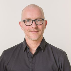 Prof. Dr. Tim Gilberger: der Abteilungsleiter trägt eine schwarze Brille, Glatze und ein schwarzes Hemd vor einem weißen Hintergrund.