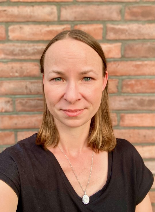 Dr. Maria Rosenthal, eine Forscherin mit mittellangen Haaren, einem schwarzen T-Shrit und Kette. Sie sieht freundlich in die Kamera.