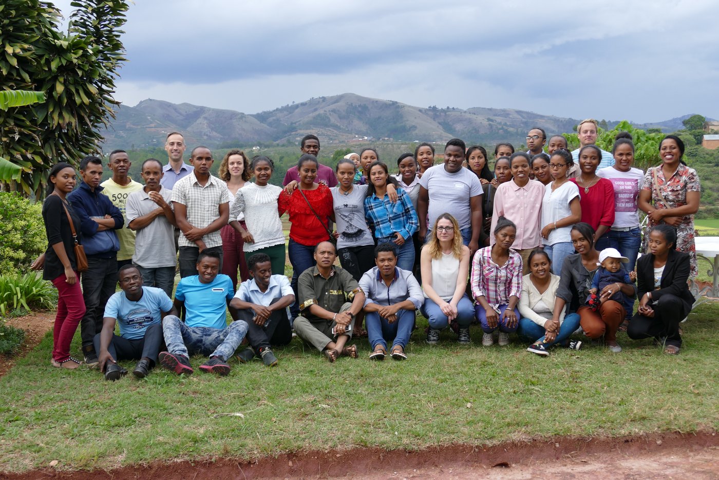A group of people from Europe and Madagascar standing or squatting together for a group photo outside in nature. They look friendly towards the viewer.