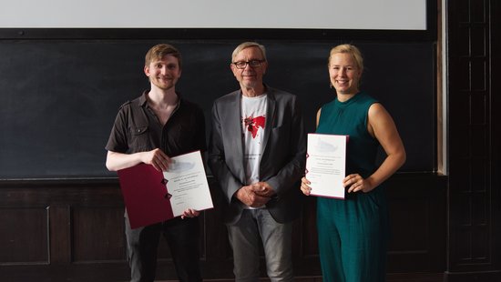 The winners of the doctoral prize stand in front of a dark background and show their certificate.