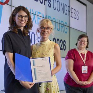 Cornelia Betsch erhält den Franz-Emanuel-Weinert-Preis. Das Foto zeigt drei Frauen schräg von links von der Seite auf der Bühne bei der Preisverleihung stehen. Vorn Cornelia Betsch mit der Urkunde in der Hand. Alle blicken freundlich in die Kamera.