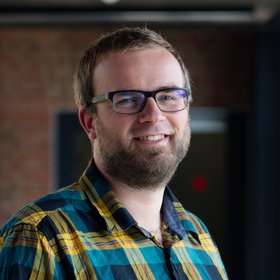 Dr Renke Lühken: a researcher wearing a green and yellow checkered shirt, short dark blond hair and a short beard.