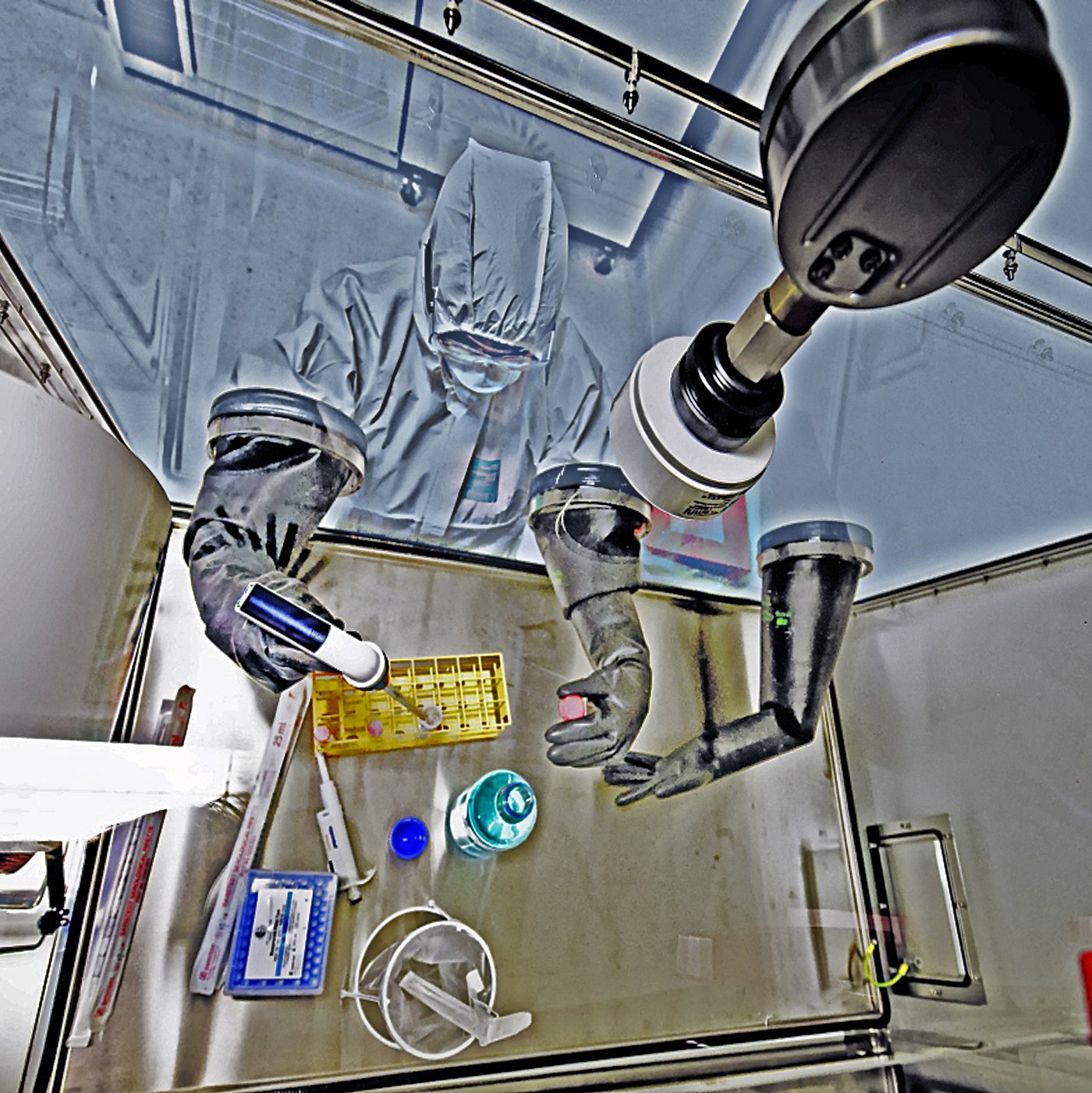 Blick von oben auf die mit Laborutensilien arbeitenden Forschenden im Vollrschutzanzug mit der sogenannten Glasbox im Hochsicherheitslabor Stufe 4