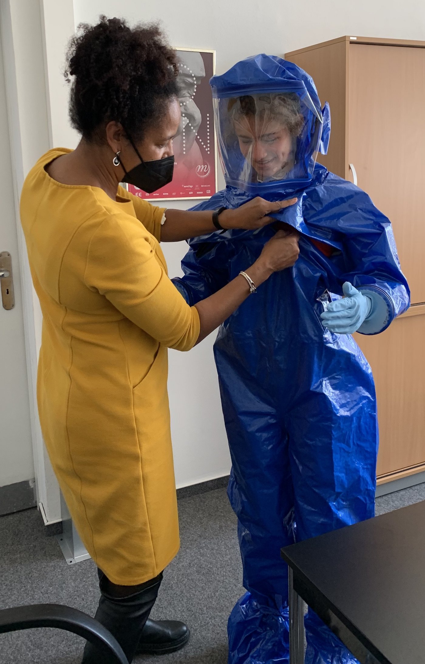 Prof. Addo hilft beim Anziehen eines blauen Sicherheitsanzugs.