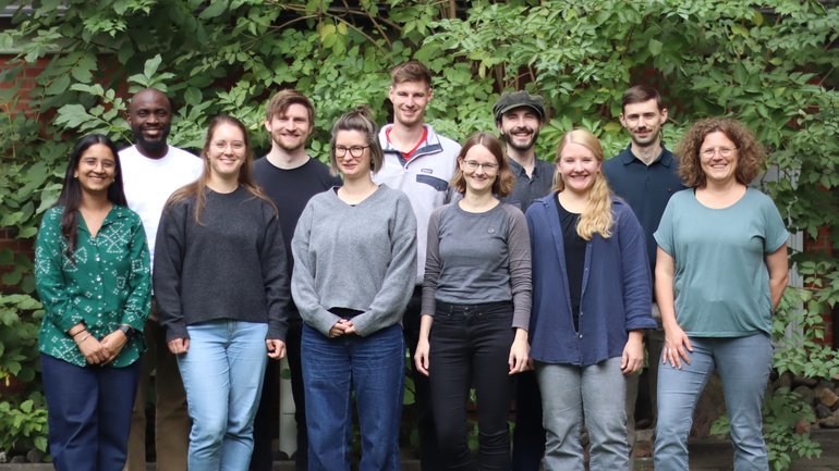 DE_2026_Gruppenfoto_Pose_1_AG-LO Die Gruppenmitglieder der Laborgruppe Oestereich posieren im Garten für ein Gruppenfoto.