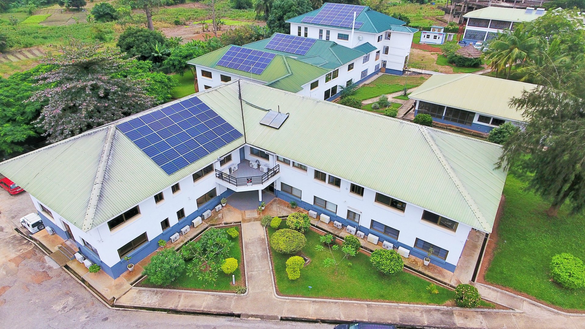 The picture shows the KCCR complex from above. You can see the green roofs of several low-rise buildings and green tropical landscape around them.