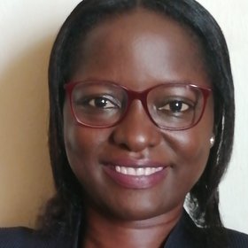 Dr Deborah Ehichioya: a researcher smiles at the camera. She wears shoulder-length black hair, red glasses and a black top.