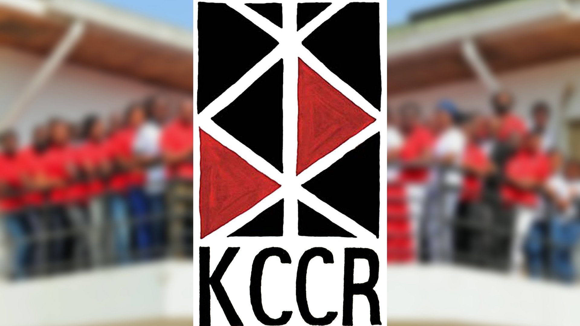 Das Bild zeigt das rot-schwarze Logo des KCCR, dahinter verschwommen die Mitarbeitenden des Instituts auf dem Instituts-Balkon.