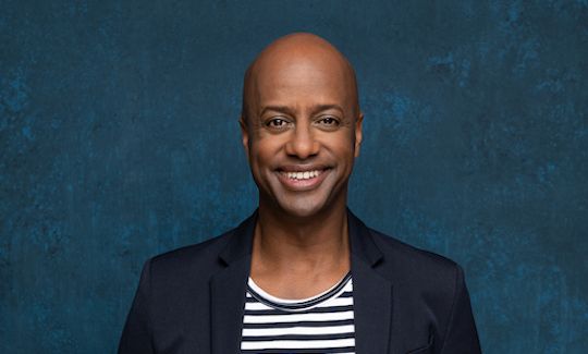 Portrait of a friendly smiling young black man without beard, bald, wearing a blue and white striped T-shirt and jacket.