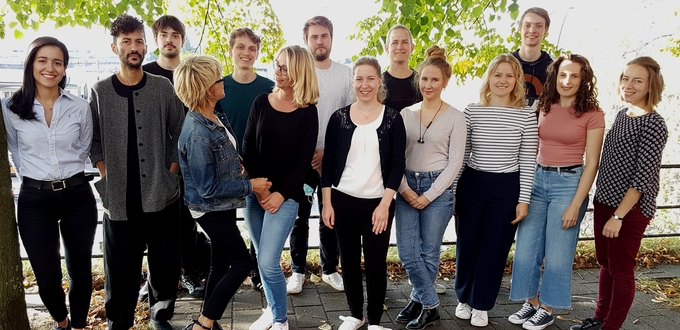 The young researchers of the Malaria cell biology group are seen taking a group photo outside, looking happily at the viewer and at each other.